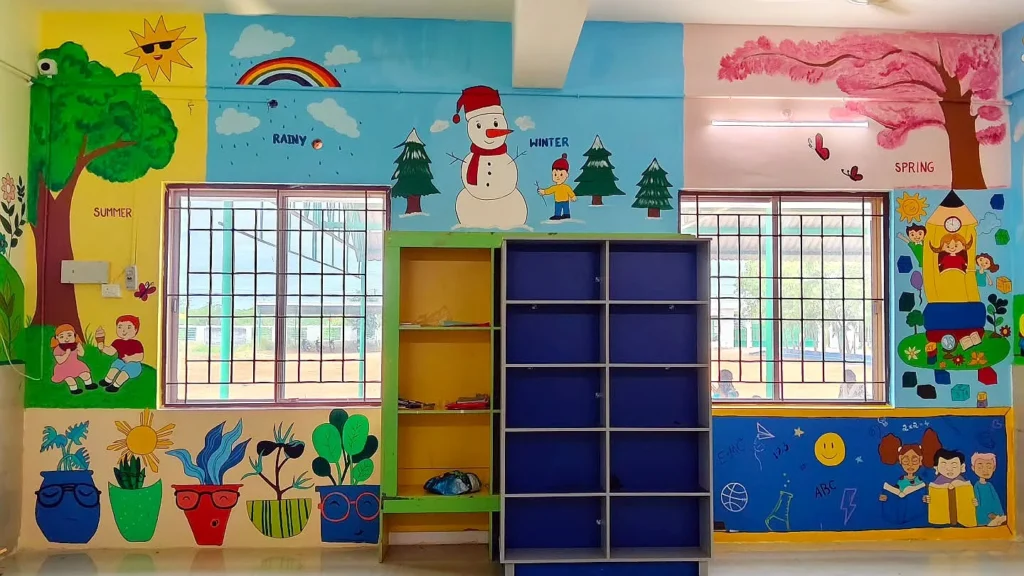 Snowman and pine trees painted above classroom cupboards — school wall painting in Sivakasi by Bhuvi